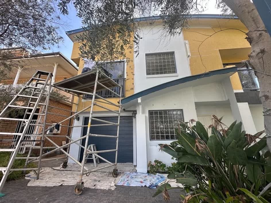 Yellow rendered house mid-repaint, with scaffolding at the front