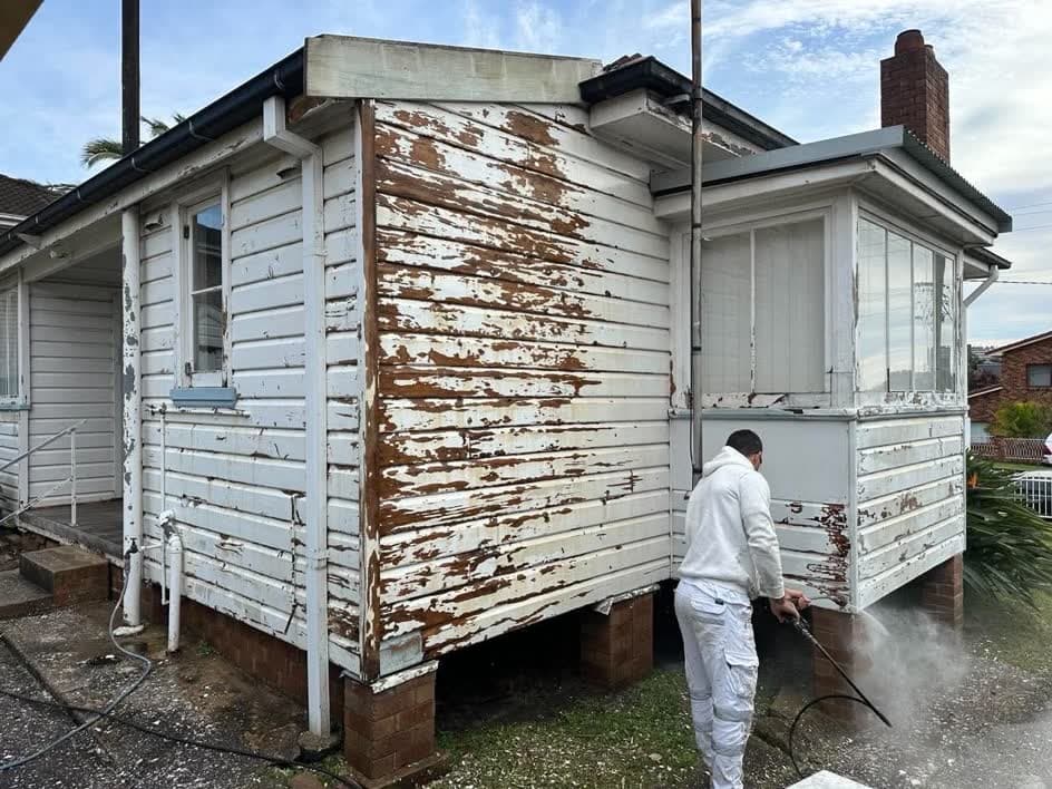 Weatherboard house with badly peeling paint, being pressure washed